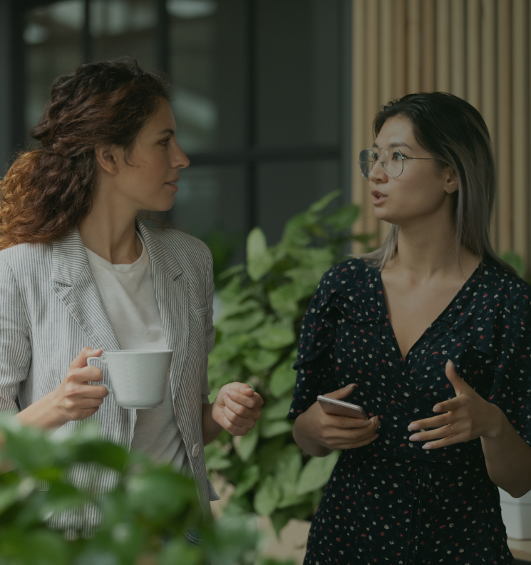Two women having a conversation while walking, holding a mug.