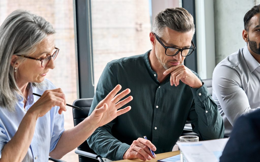 A group of three people having a conversation and looking at a laptop.