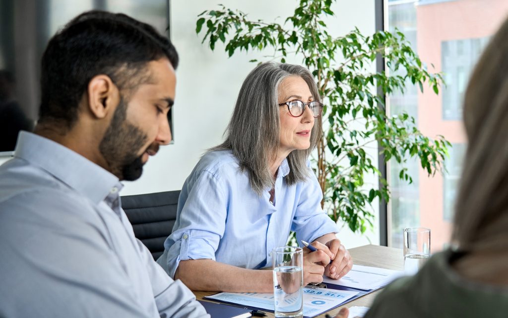 People having a conversation in a conference room. There are glasses of water on the table and charts and graphs.